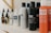 A variety of haircare products are displayed on a shelf. The prominently visible bottles feature different types of sprays and oils with bold labels. The products are arranged in a neat line, showcasing their branding and color schemes.