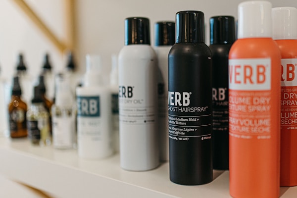 A variety of haircare products are displayed on a shelf. The prominently visible bottles feature different types of sprays and oils with bold labels. The products are arranged in a neat line, showcasing their branding and color schemes.