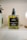 A rectangular glass bottle of body oil labeled 'little barn apothecary HONEYSUCKLE + GRAPEFRUIT BODY OIL' with a black pump on top. The bottle contains a yellow-green liquid and is placed on a shelf with a blurred background.
