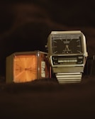 Two digital wristwatches are displayed with an emphasis on their vintage designs. The watch on the left has an orange face with a simple, classic design, while the watch on the right features a black face with a digital screen displaying the time, along with additional features. Both have metallic casings with a retro aesthetic.