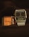Two digital wristwatches are displayed with an emphasis on their vintage designs. The watch on the left has an orange face with a simple, classic design, while the watch on the right features a black face with a digital screen displaying the time, along with additional features. Both have metallic casings with a retro aesthetic.