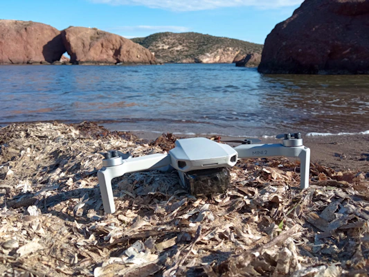DJI Mini drone resting on a sandy beach with clear blue skies.