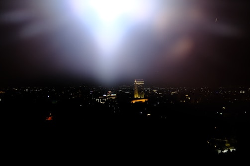 A shadowed cityscape at night with golden light beams cutting through the dark sky.