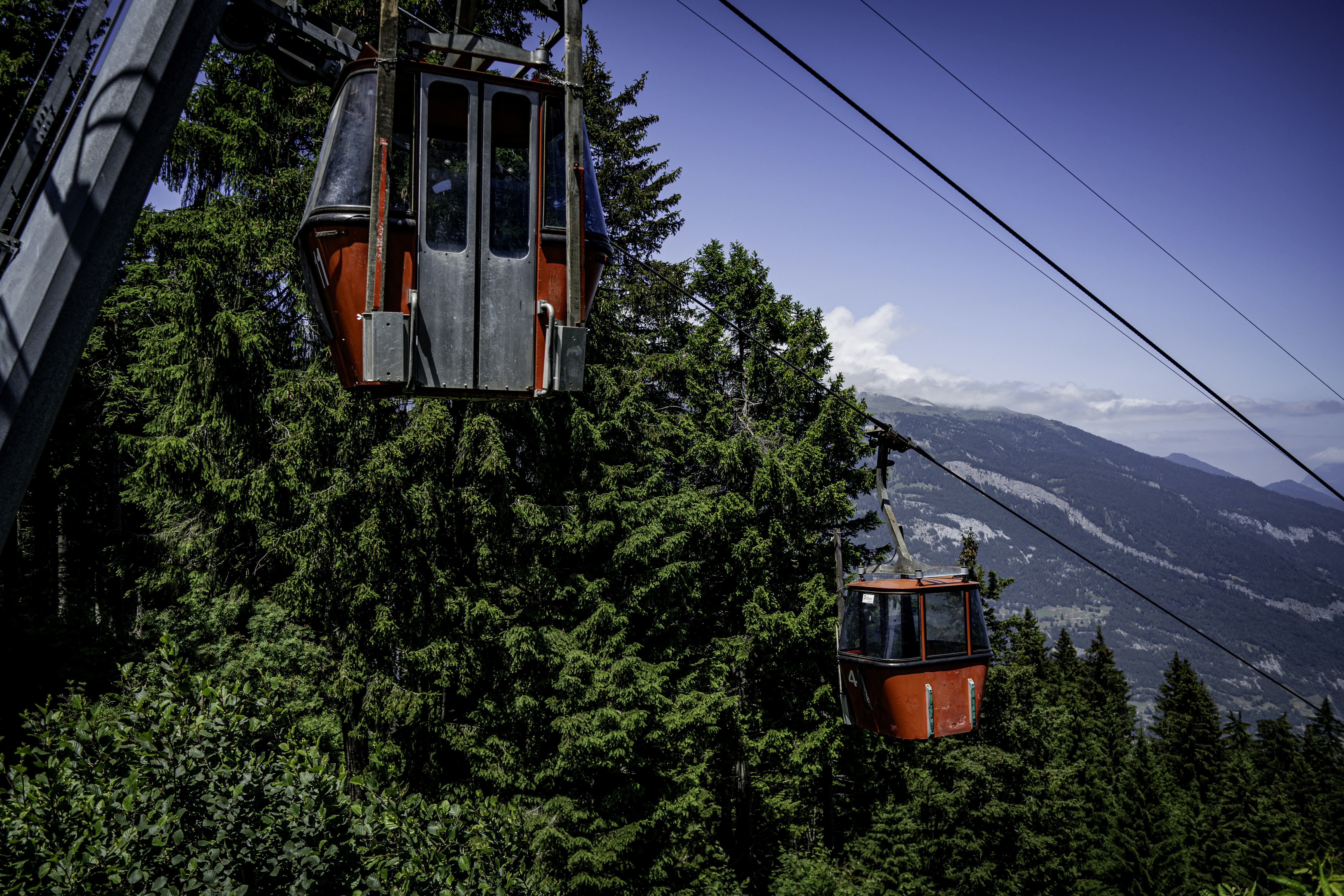 a couple of people riding a ski lift over a forest
