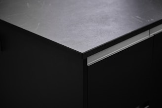 Close-up of a sleek, polished quartz countertop in a sunlit modern kitchen with black and gold accents.