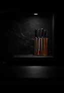 A set of polished kitchen knives arranged neatly on a wooden cutting board with fresh vegetables