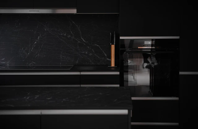 A black kitchen with marble counter tops and black cabinets