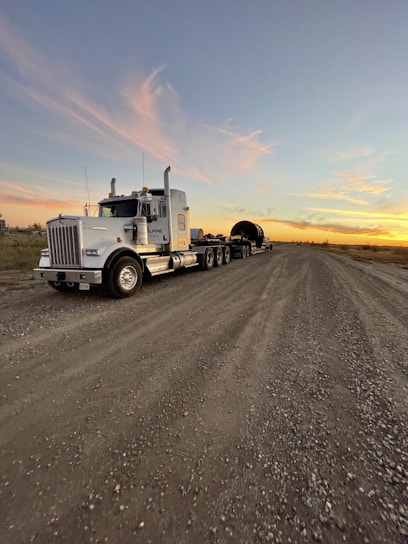 An energetic owner-operator reviewing load options on a tablet, with a loaded semi-truck ready to roll in the background at sunset.