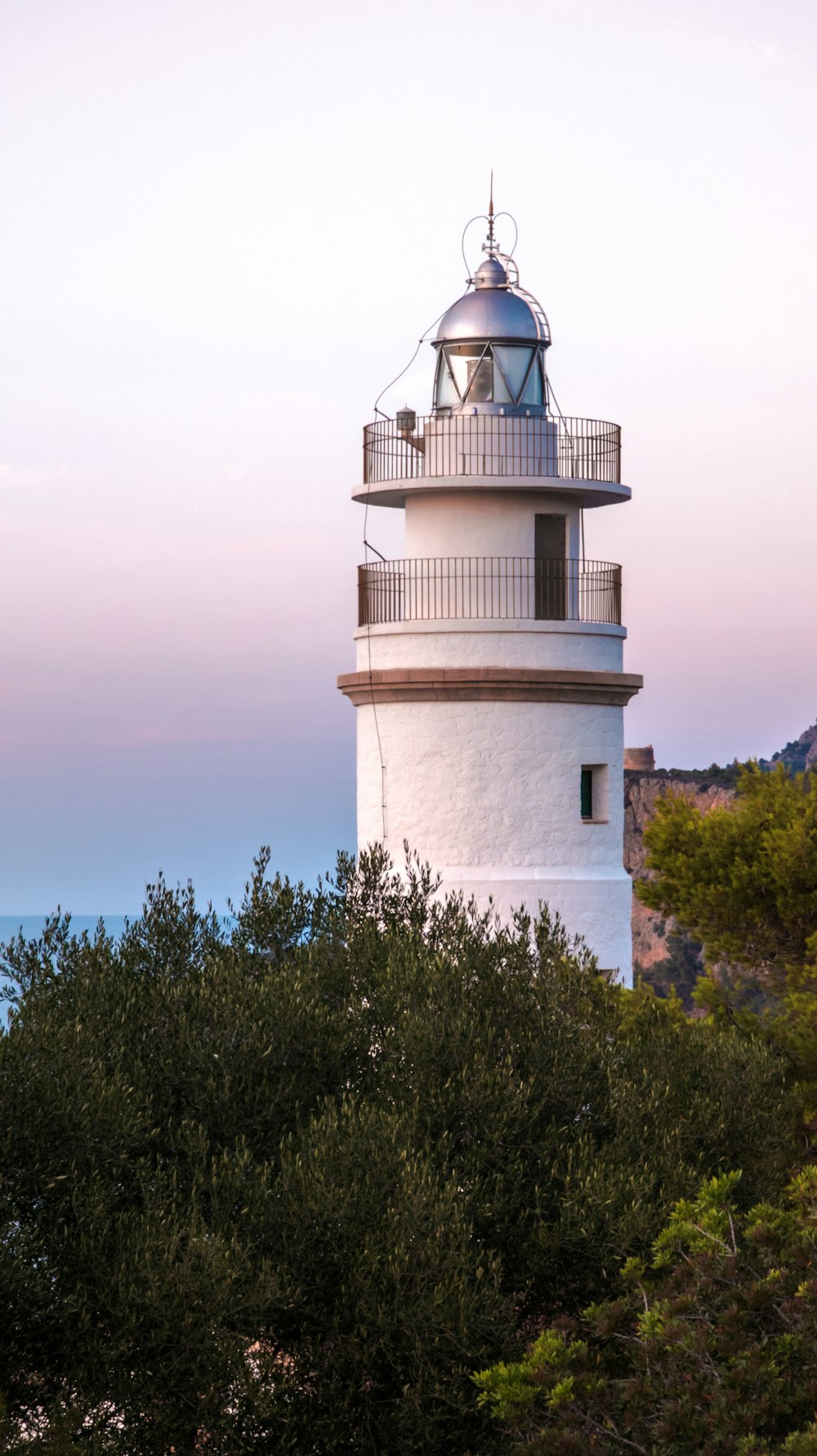 a white light house sitting on top of a lush green hillside