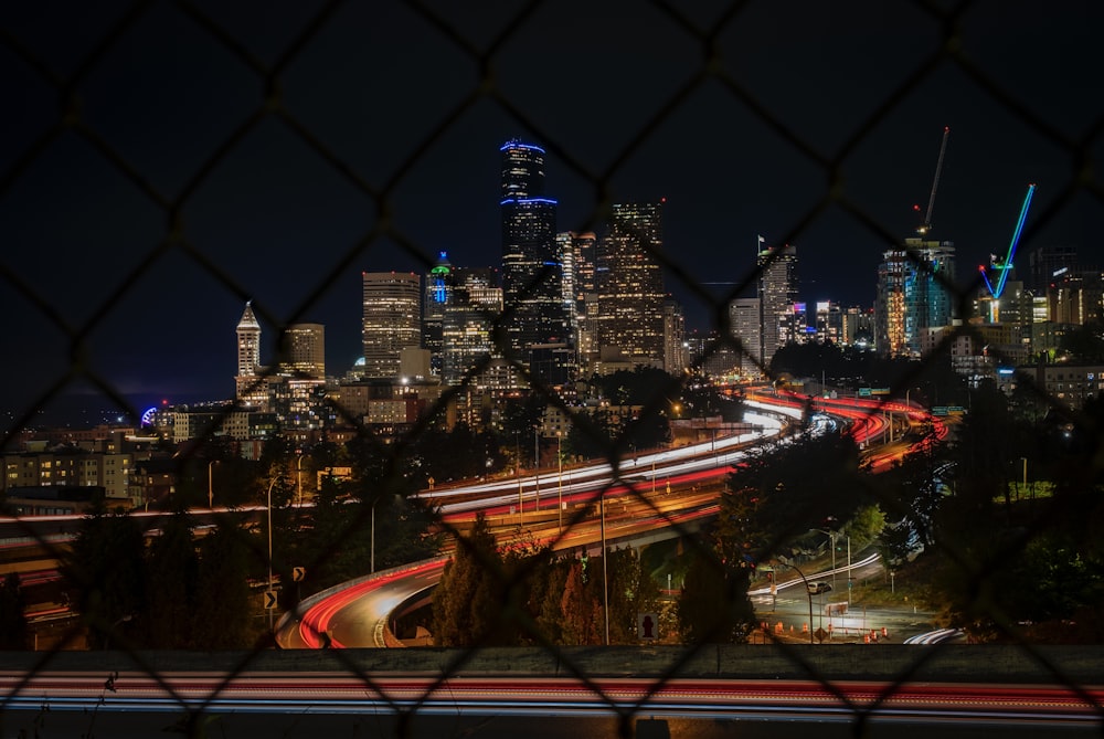 Una vista de una ciudad por la noche a través de una cerca de alambre