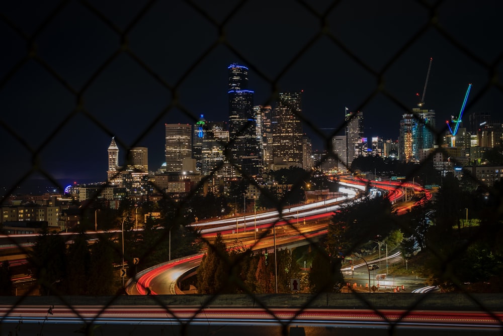 a view of a city at night through a chain link fence