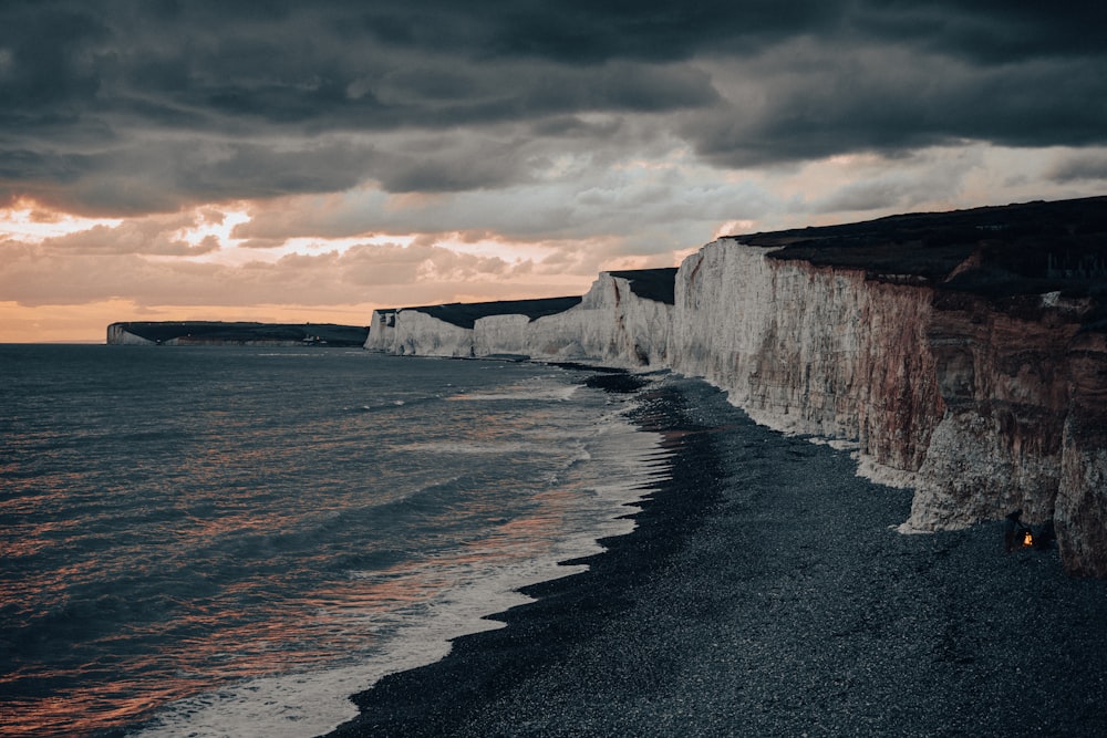 a beach next to the ocean with a cliff in the background