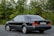 A classic black sedan is parked on an asphalt surface with lush green foliage in the background. The vehicle is well-kept, featuring a sleek design, tinted windows, and distinctive branding on the rear. The license plate is visible, adding to the detailed appearance of the car.