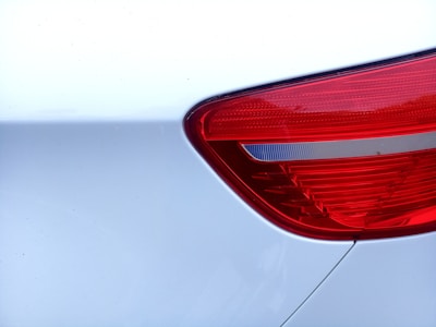 Close-up view of a car's rear light assembly with a shiny red plastic cover set against a smooth white car body.