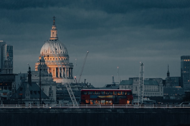 a red double decker bus driving past a tall building