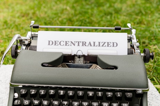 A vintage typewriter with the word 'DECENTRALIZED' typed on a sheet of paper. The typewriter is positioned outdoors on a grassy surface.
