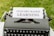 A vintage typewriter with a white paper inserted into it is displayed. The paper has the phrase 'INQUIRY-BASED LEARNING' typed in bold letters. The typewriter is set on a green grassy background.