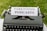 A vintage typewriter with a piece of paper in it, displaying the words 'Parenting Podcasts'. The typewriter is set on a grassy surface.