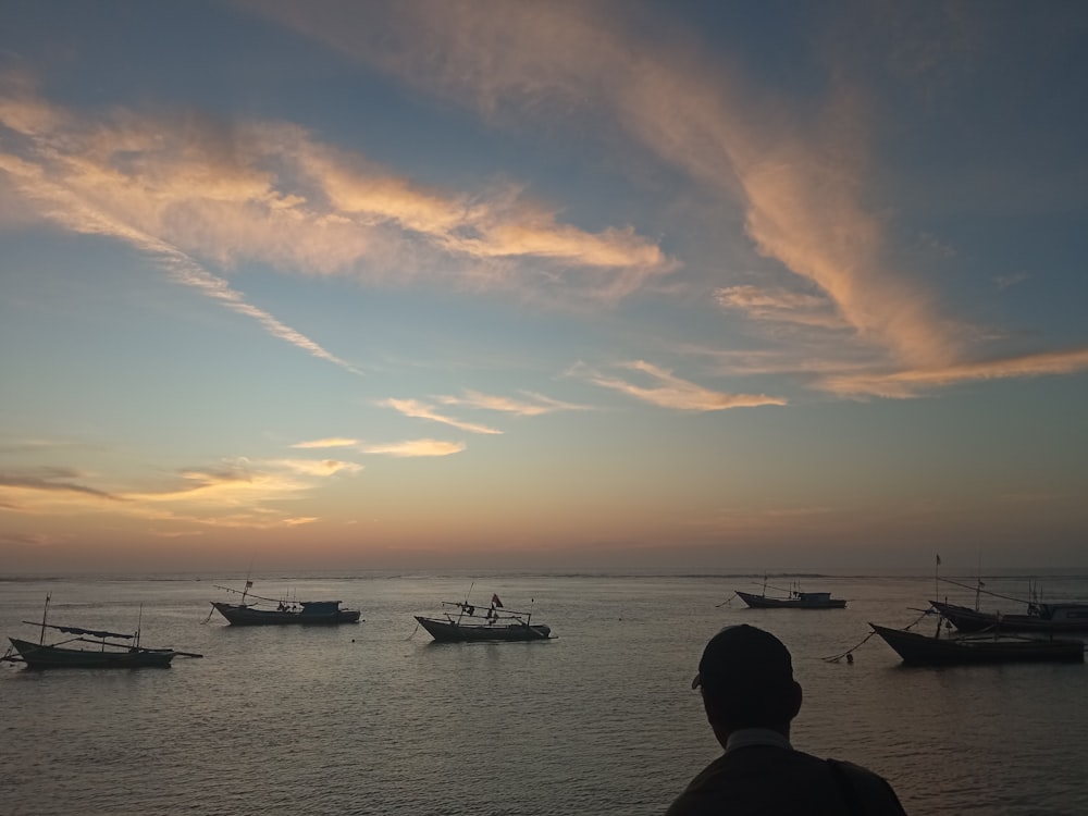 a man standing on a beach watching boats in the water