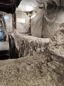 The interior features walls and ceilings covered with salt or a mineral-like substance, creating a textured, crystalline appearance. There is a wooden structure in the middle that could be a walkway or railing. Soft lighting provides a subtle glow, highlighting the rugged surface details.