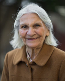 An elderly white woman with grey hair smiling warmly as she steps out of a Coastal Care Transport vehicle.