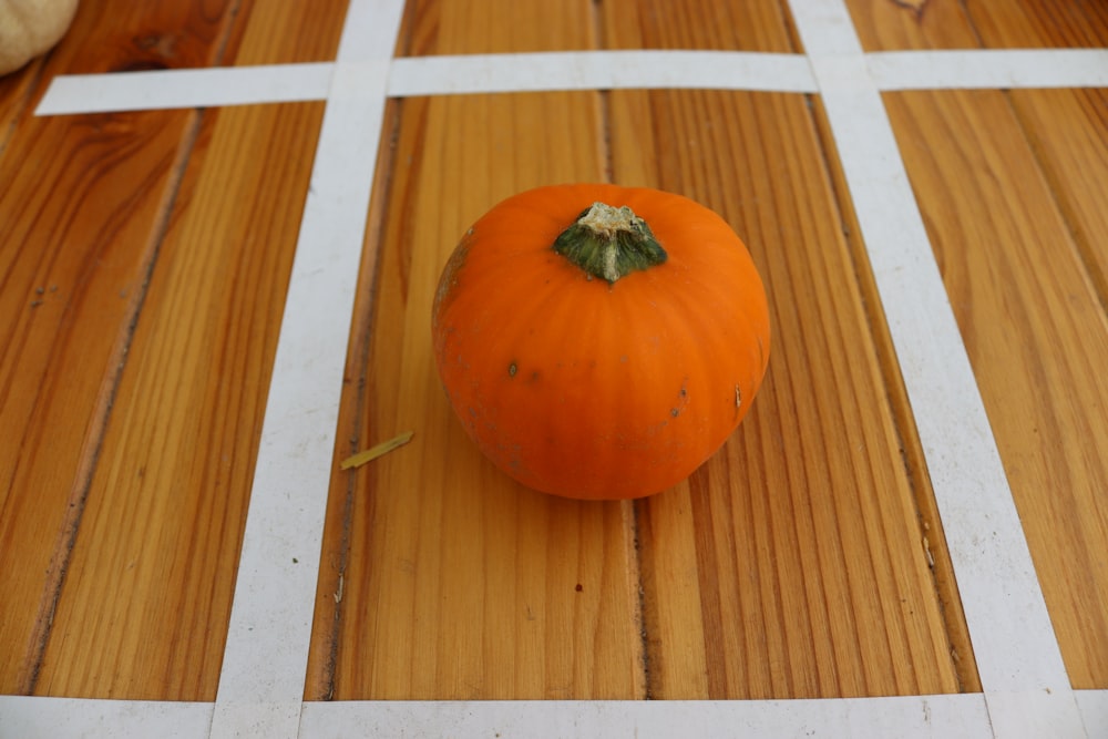 una piccola zucca arancione seduta su un pavimento di legno