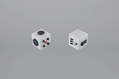 Two fidget cubes with various tactile components are displayed against a plain background. Each cube features a different arrangement of buttons, dials, and switches designed for sensory interaction.