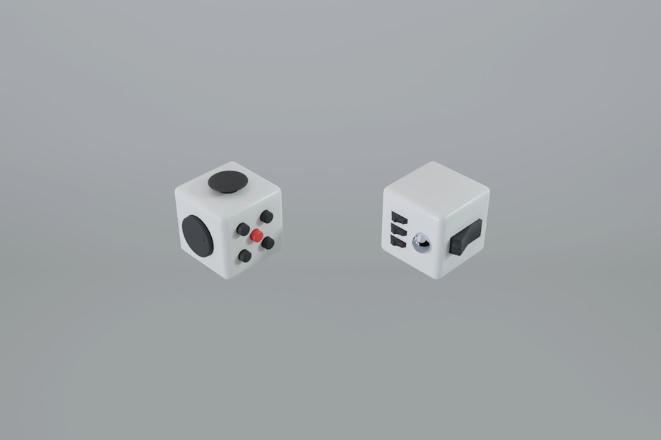 Two fidget cubes with various tactile components are displayed against a plain background. Each cube features a different arrangement of buttons, dials, and switches designed for sensory interaction.