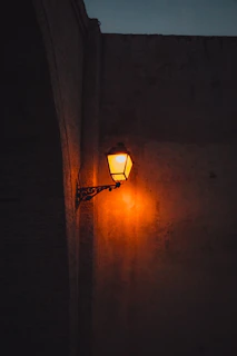 A sleek metal hook mounted on a textured stone wall, holding a hanging lantern softly glowing.