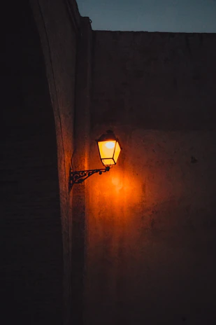 A sleek metal hook mounted on a textured stone wall, holding a hanging lantern softly glowing.