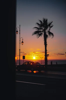 The sun setting behind a coastal highway with a silhouette of a tuk-tuk headed toward the horizon.