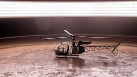A small helicopter model placed on a textured brown surface under a bright, blurred horizontal light streak. The helicopter is detailed with visible rotors and a clear cockpit.