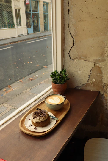 Cozy café corner with a beautifully decorated cake and a steaming cup of coffee on a wooden table.