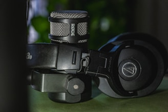 A close-up view of a professional microphone and a pair of over-ear headphones. The microphone has a metallic grille with the brand name visible, while the headphones feature cushioned earpieces and an adjustable headband.