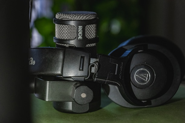 A close-up view of a professional microphone and a pair of over-ear headphones. The microphone has a metallic grille with the brand name visible, while the headphones feature cushioned earpieces and an adjustable headband.