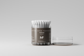 An open plastic container filled with cotton swabs is set against a minimalist background. The packaging is labeled with text including 'cotton swab packaging' and 'mockups'. The container is transparent with a muted, dark label and there is a separate flat lid placed beside it.
