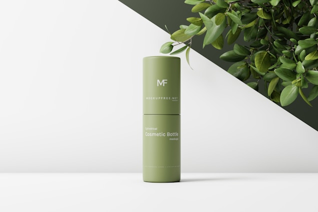 A green cylindrical cosmetic bottle with text on its surface, positioned on a minimalist white and dark green background. There are some leafy branches in the top right corner, adding a natural element to the composition.
