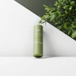 Elegant glass bottle of hydrating serum with fresh botanical leaves around it on a marble surface.