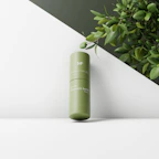Elegant glass bottle of hydrating serum with fresh botanical leaves around it on a marble surface.