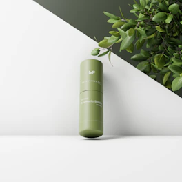 A sleek bottle of facial serum with droplets on the surface, placed next to fresh green leaves.