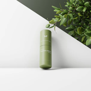 A sleek bottle of facial serum with droplets on the surface, placed next to fresh green leaves.