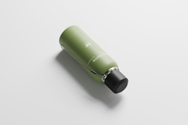 A sleek, modern water bottle lying on its side with a green body and a black cap. The surface is matte, and there are writings on the bottle near the top. The background is a clean, minimalist white, highlighting the bottle's design.