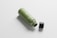 A reusable green water bottle lies on its side with a black screw-on cap beside it. The bottle features a subtle design with a silver handle attached to its neck.