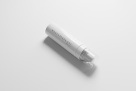 A white cylindrical bottle with a clear cap, featuring the text 'MOCKUPFREE.NET' printed on it, placed on a light grey background with a soft shadow.