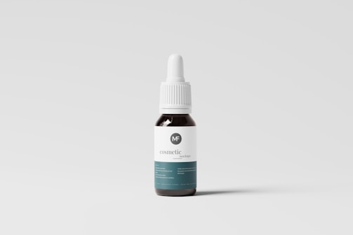 A small dropper bottle with a dark body and a white label featuring minimal text and a logo. The bottle has a white screw-on dropper cap, and it is positioned against a plain, light-colored background.