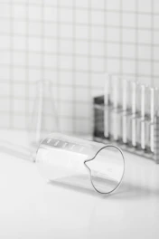 Close-up of a scientist carefully inspecting a clear glass beaker in a bright laboratory.