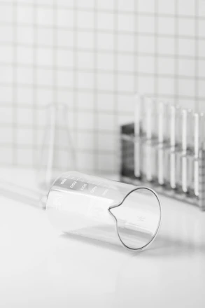 Close-up of a scientist carefully inspecting a clear glass beaker in a bright laboratory.