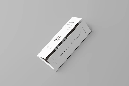 A white tri-fold pamphlet with a minimalist design placed on a light gray background. The pamphlet features bold, black typography with the letters 'MF' prominently displayed. The text 'MOCKUPFREE.NET' is visible, along with some smaller text details. The pamphlet appears sleek and professional.