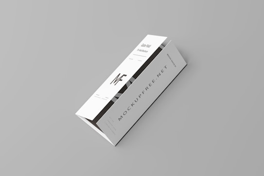 A white tri-fold pamphlet with a minimalist design placed on a light gray background. The pamphlet features bold, black typography with the letters 'MF' prominently displayed. The text 'MOCKUPFREE.NET' is visible, along with some smaller text details. The pamphlet appears sleek and professional.