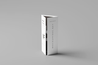 A folded paper brochure with a minimalist design is placed upright against a neutral background. The brochure has text elements, including a bold 'MF' logo and vertical text 'MOCKUPFREE.NET.'